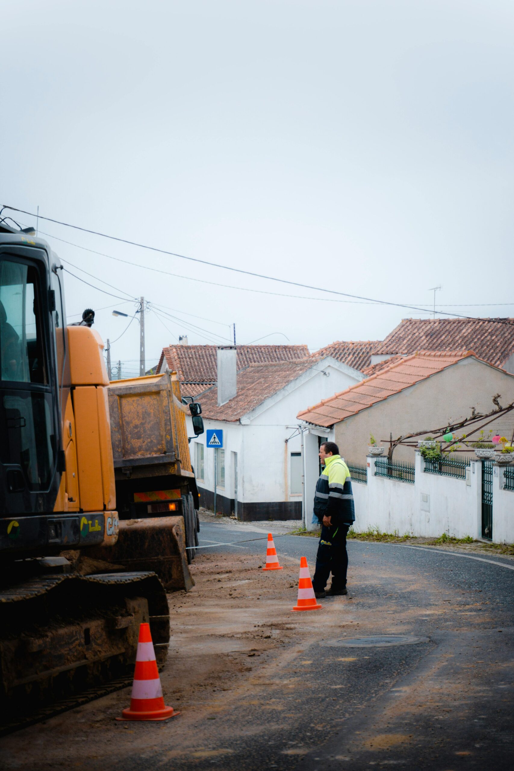 A road construction site in a suburban area with equipment and a standing worker.
